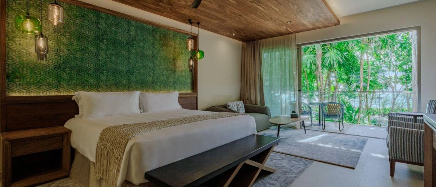 Nature-inspired hotel room with neutral tones, an earth-green wall mural, a wooden ceiling and patio doors that open to a furnished balcony overlooking the mangroves