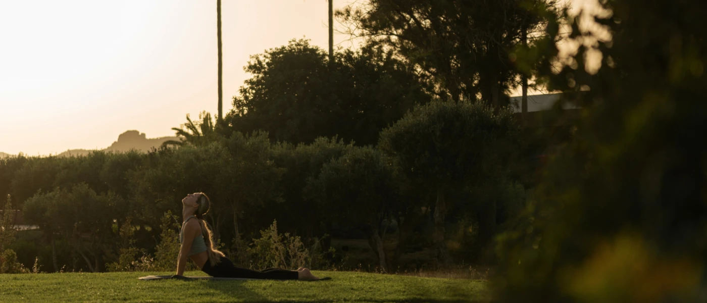 Woman in leggings and a gym top in a yoga pose on a mat in a lush garden