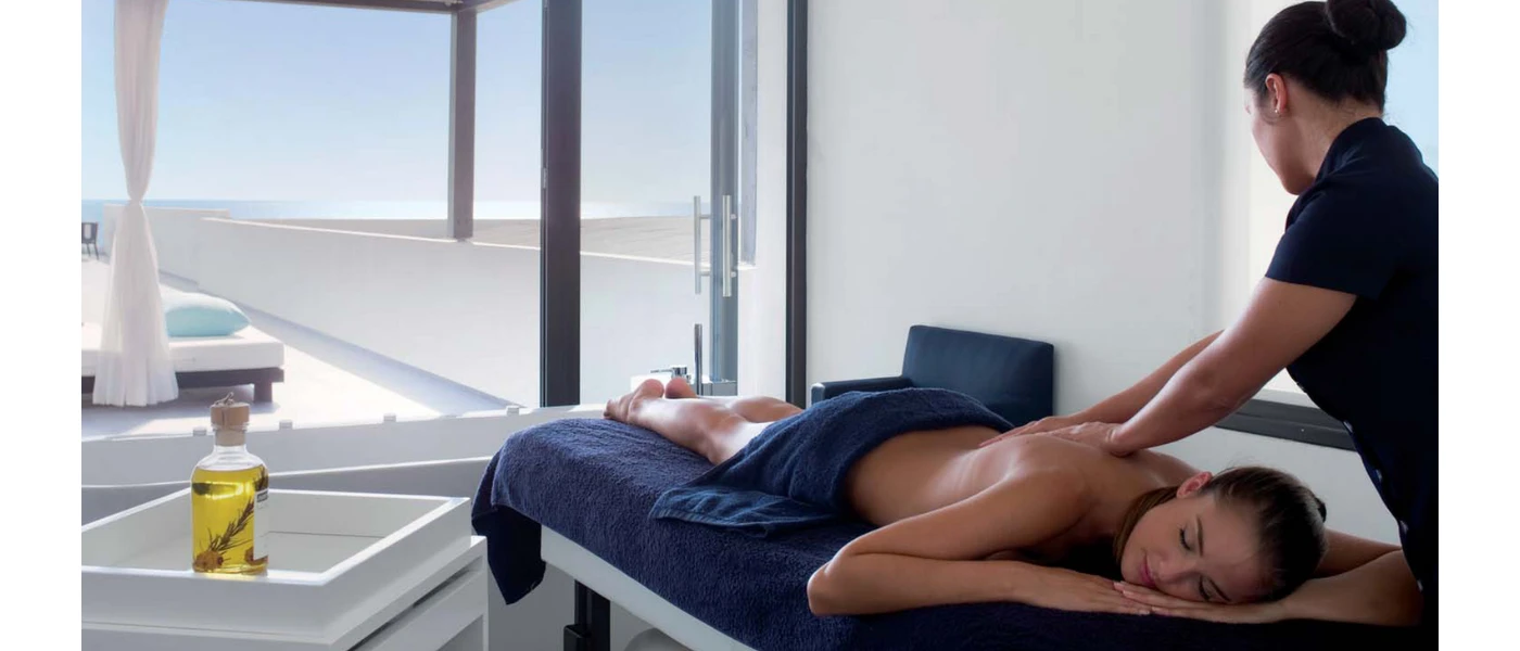 Woman lying down in a sea-facing treatment room enjoying a massage from a therapist in uniform