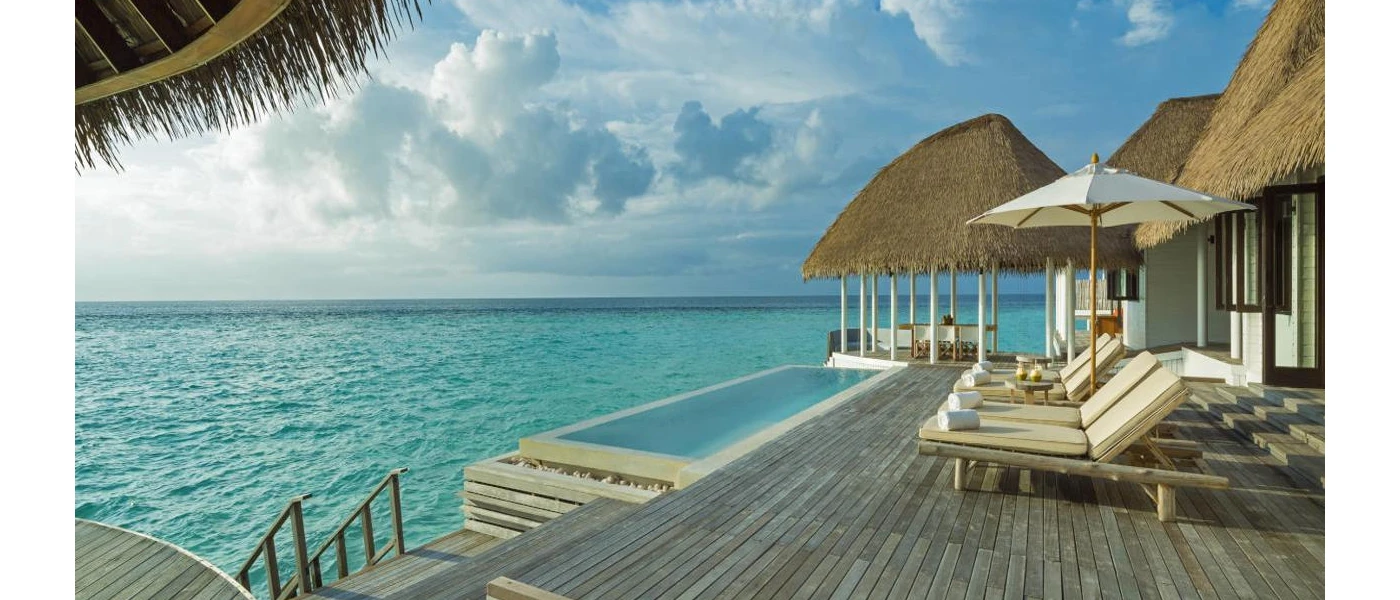 Thatched-roof villa with a wooden sundeck, ivory-cushioned loungers, a private pool and steps down into the sea