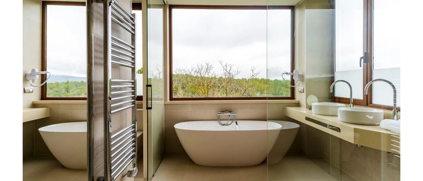 Modern bathroom with neutral vanity unit, walls and a white bathtub with a large window overlooking the countryside