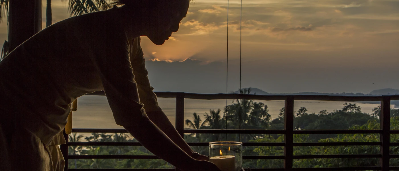 Staff member lights a candle on a table in an open-air pavilion with a sea view