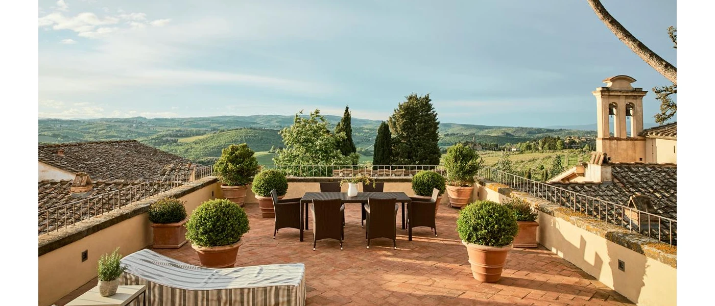 Concrete patio rooftop above tiled roofs, with terracotta potted plants and a view of the surrounding countryside
