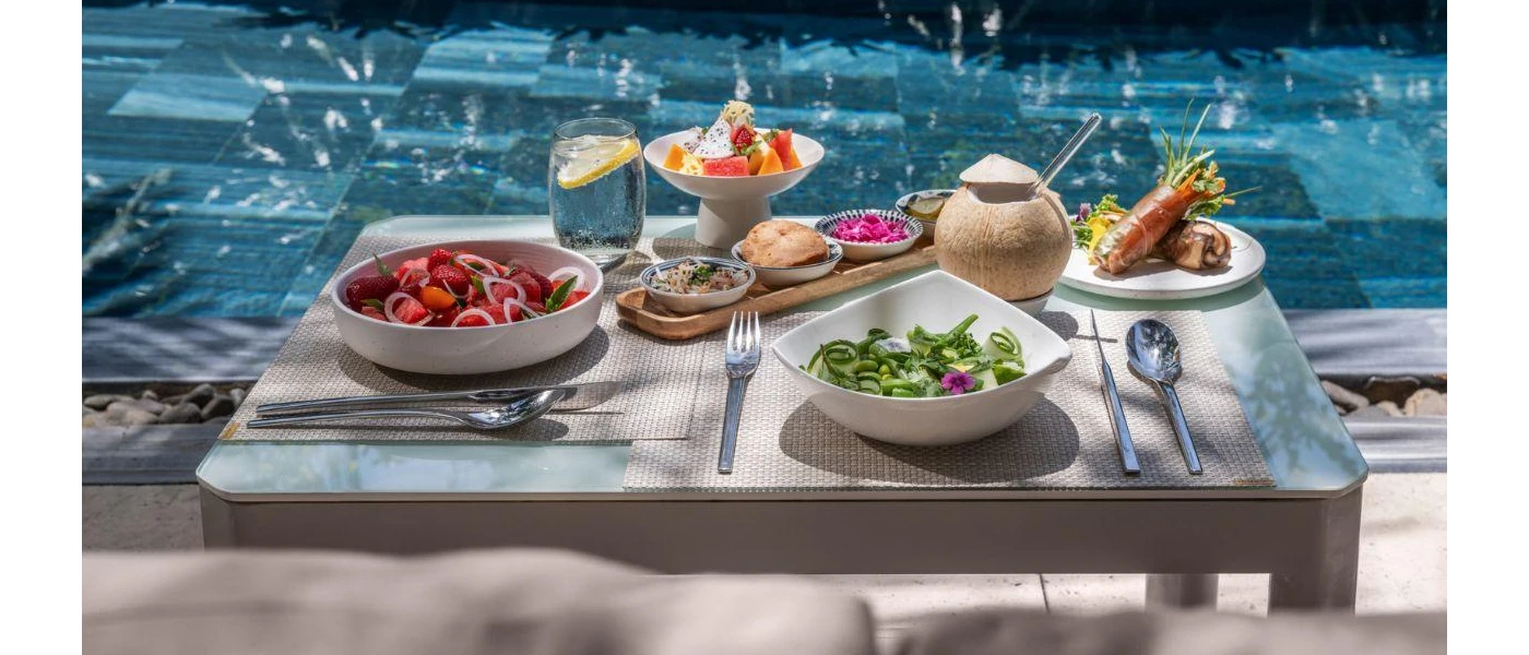 Tray of nutritious, colourful food laid out on a poolside, including a green salad, edible flowers, and fresh fruit