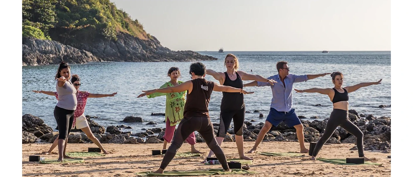 Group practice yoga on the shoreline with the waves and green hillsides in the background