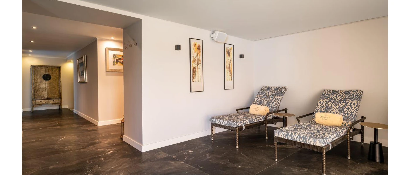 White room with grey tiled floors, loungers with blue and white patterned cushions and framed abstract art on the walls