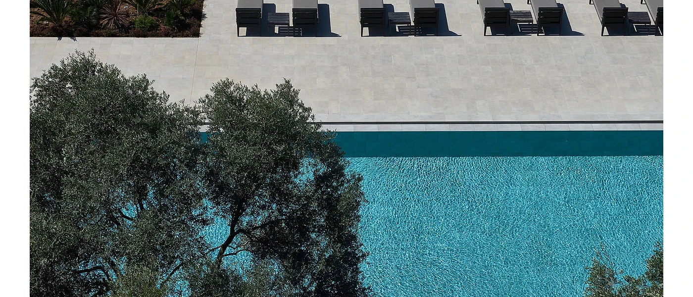 Aerial view of a swimming pool, treetop and paved terrace with cushioned sun loungers