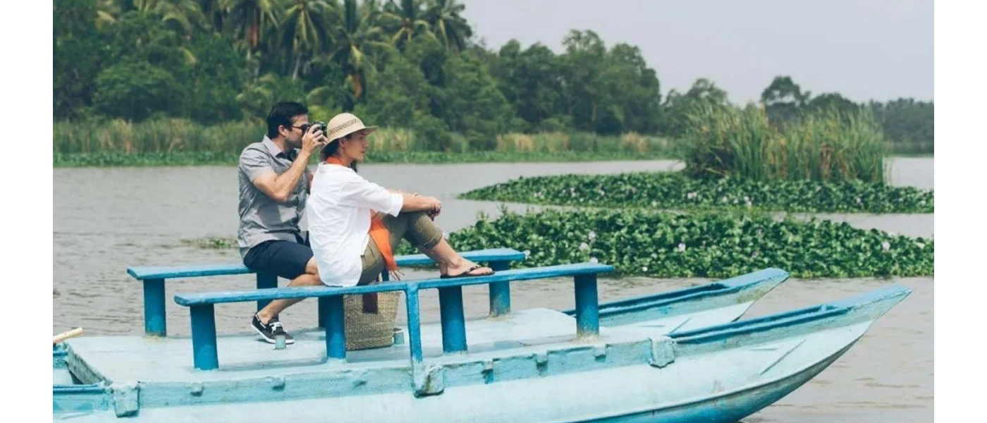 Man and woman enjoying the view of surrounding water and tropical greenery in a wooden boat