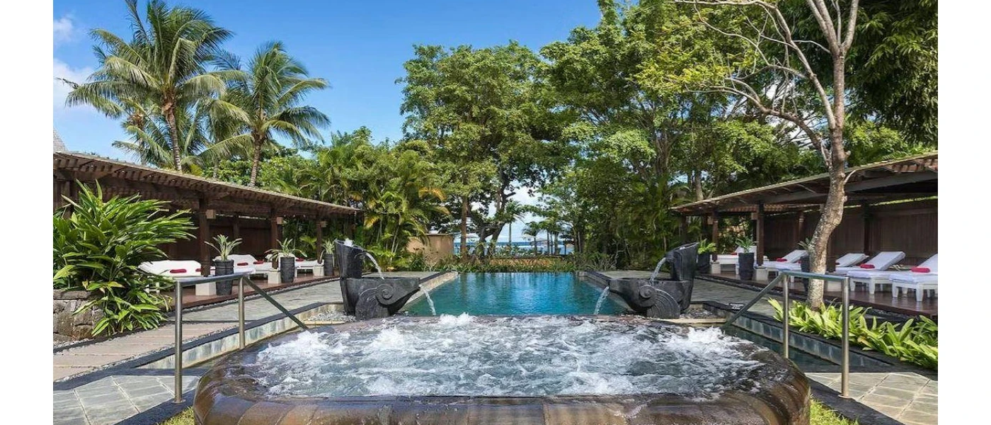 Outdoor pool overlooking the sea with an elevated whirlpool bath, surrounded by white daybeds with red cushions 