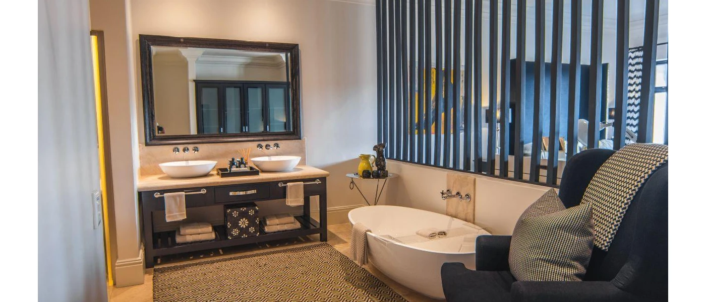 Modern bathroom with a white tub, dark-wood mirror and vanity unit, and a charcoal armchair, with panels that see through to the bedroom