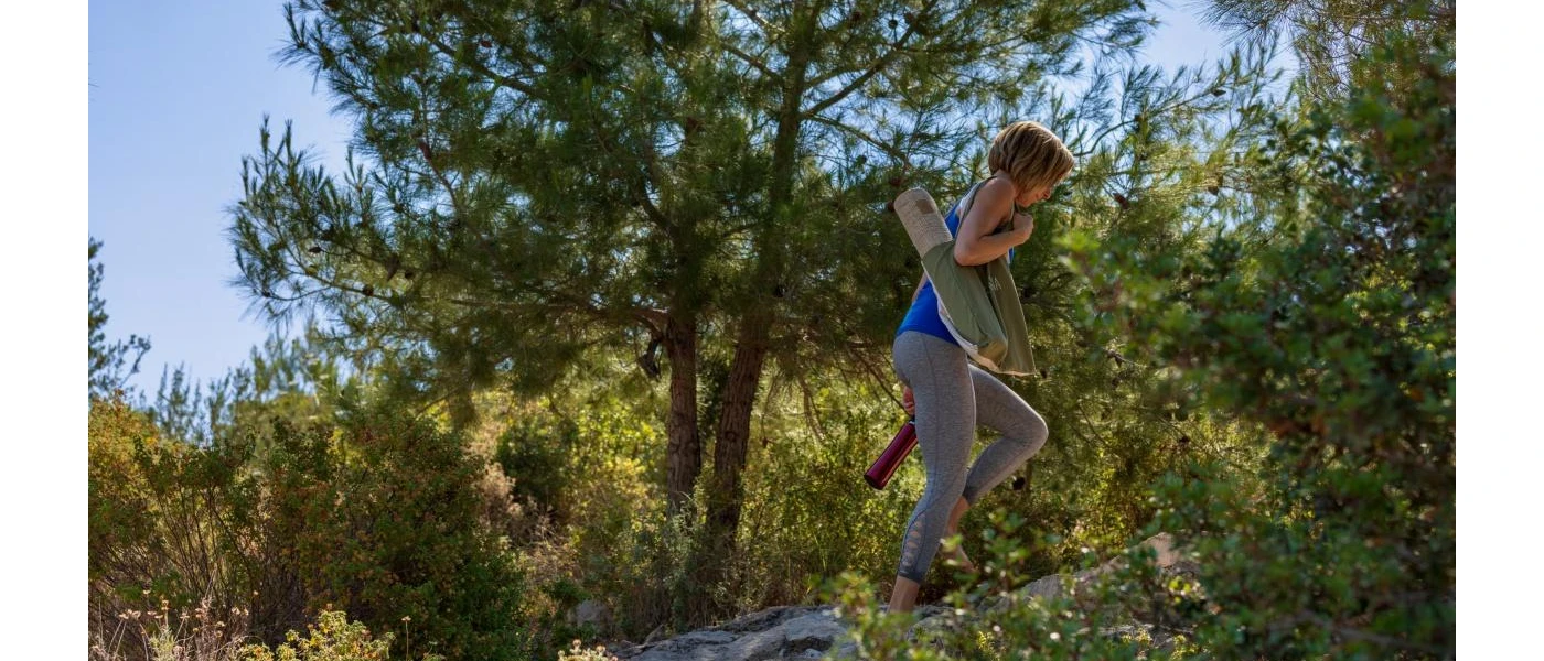 Woman in active wear walking up a hill among greenery under a blue sky