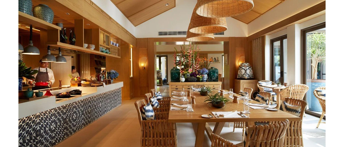 Stylish dining area with a wooden table, rattan lantern-style ceiling lights, and a show cooking station with chefs hard at work