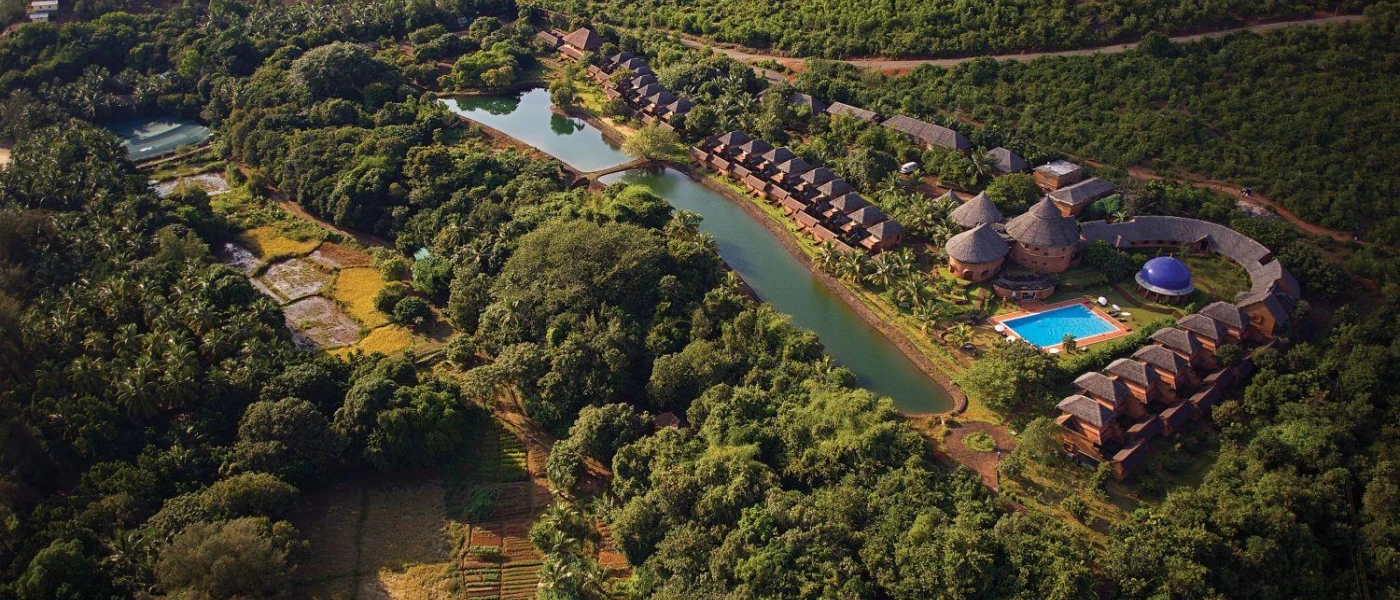 Traditional wooden huts and buildings with thatched roofs, surrounded by coconut groves and overlooking a lake