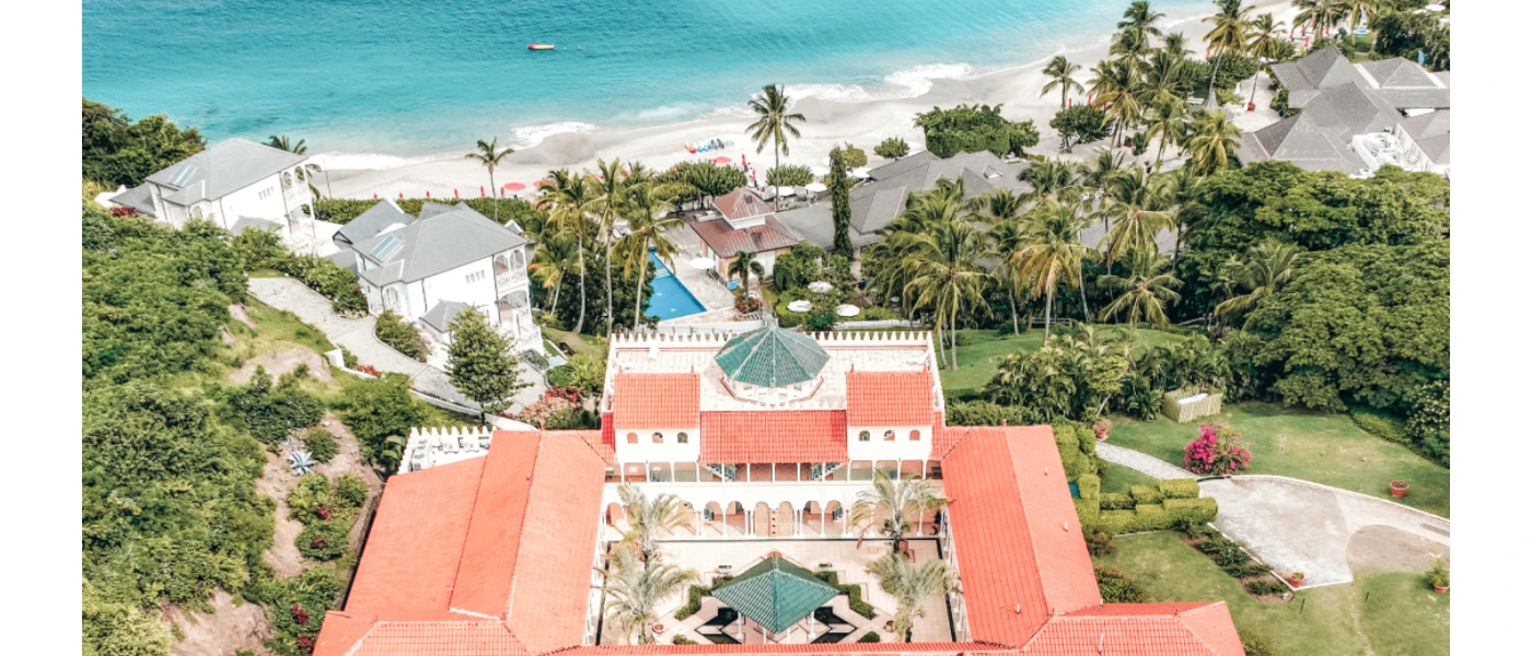 Red and grey rooftops among lush tropical greenery and overlooking a white-sand beach