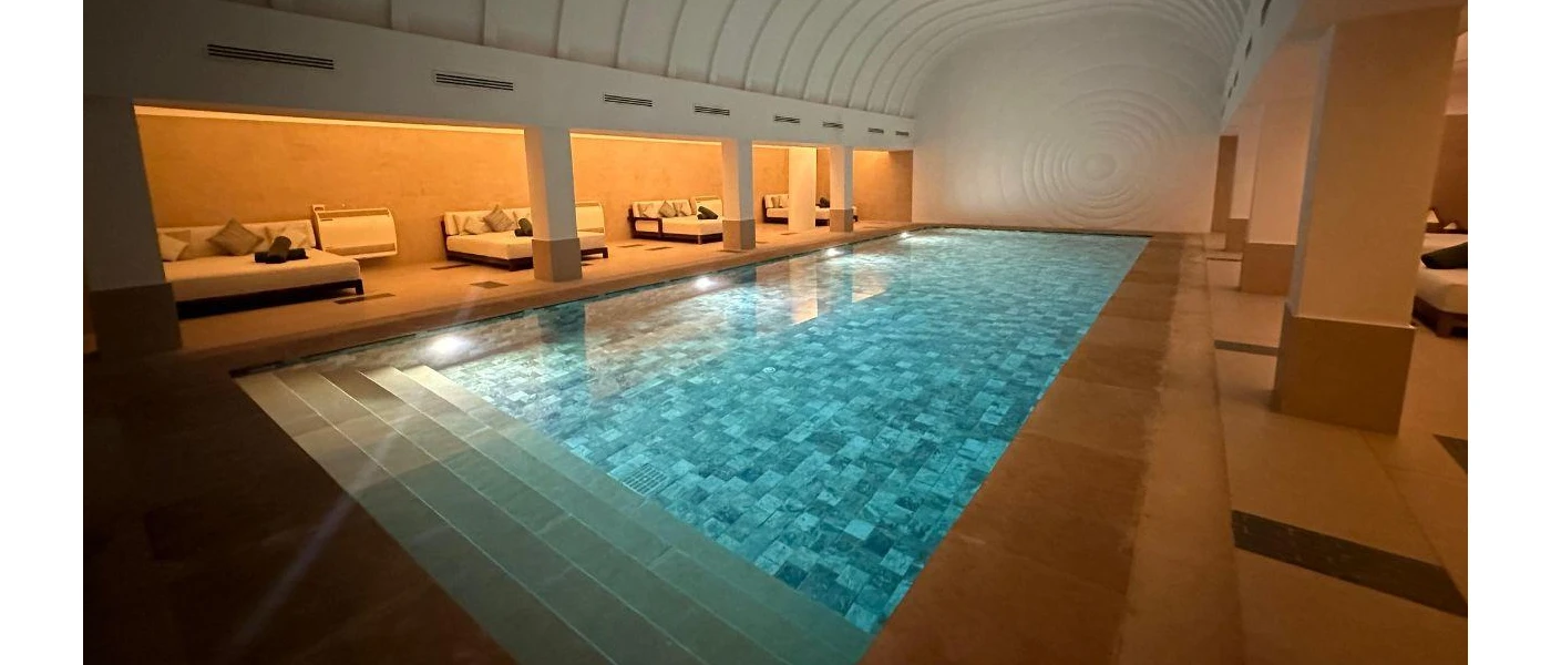 Indoor swimming pool with underwater lighting, surrounded by white daybeds