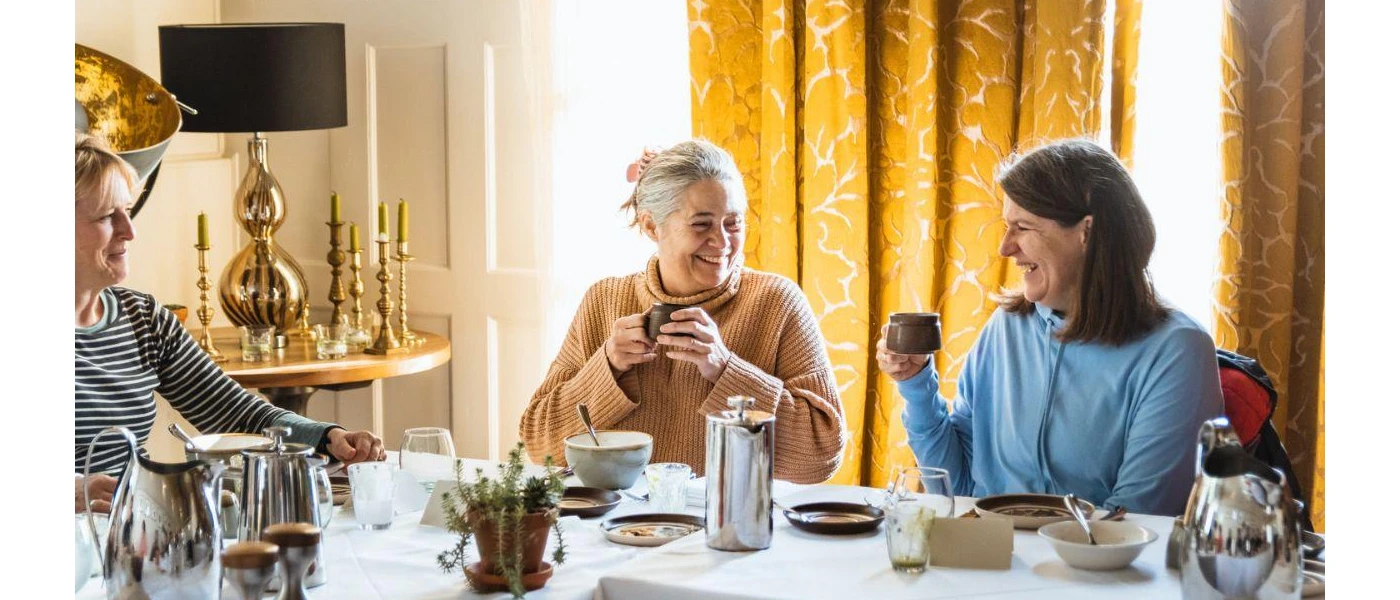 Three ladies sitting around a white table holding cups and smiling