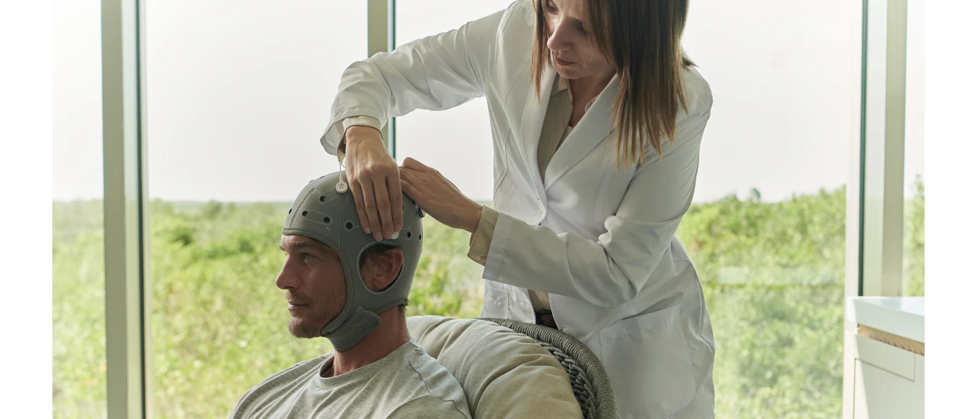 Man sitting in a chair with an apparatus on his head as a health expert fixes it on