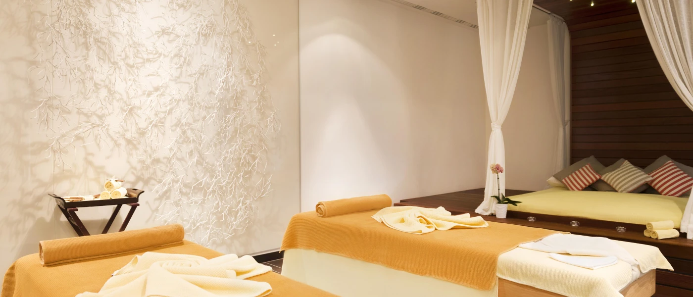 Room with neutral walls, yellow massage beds and white draped fabric, in a wellness setting