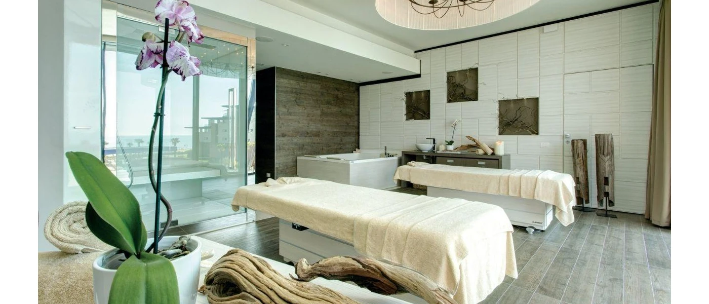 Rustic treatment room with twin massage beds, wooden flooring and furniture, ornamental drift wood and a potted orchid