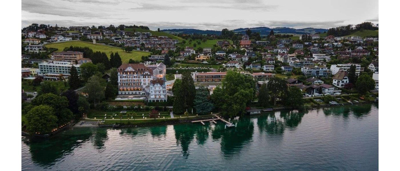 Chenot Palace from the lakefront, fronted by greenery and a wooden jetty