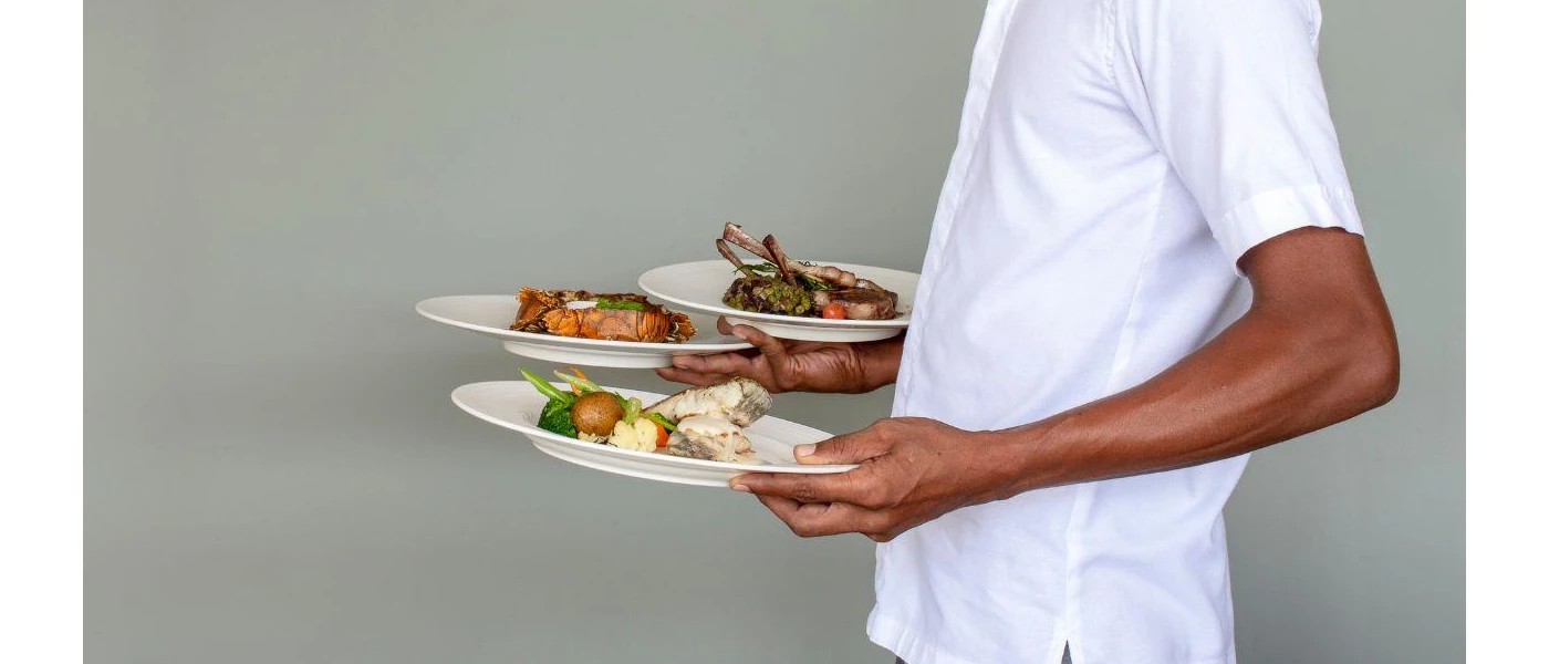 Person in white carrying plates of fish, meat and vegetables designed beautifully