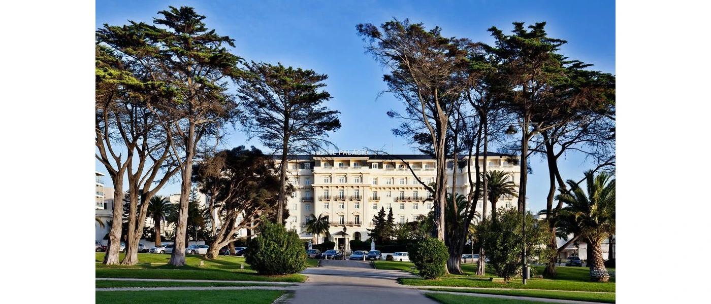 Palacio Estoril's grand white exterior, framed by greenery including tall trees under a blue sky