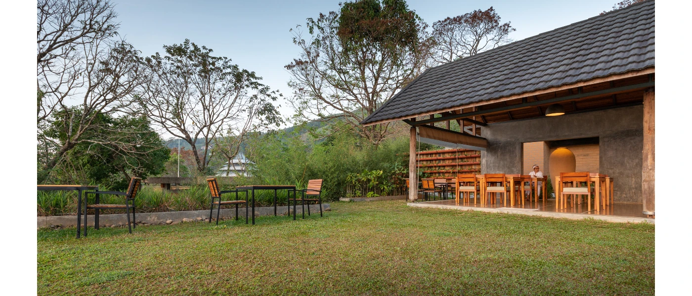Traditional building with a tiled roof, stone walls and stilts, with an outdoor seating area and grassy lawn