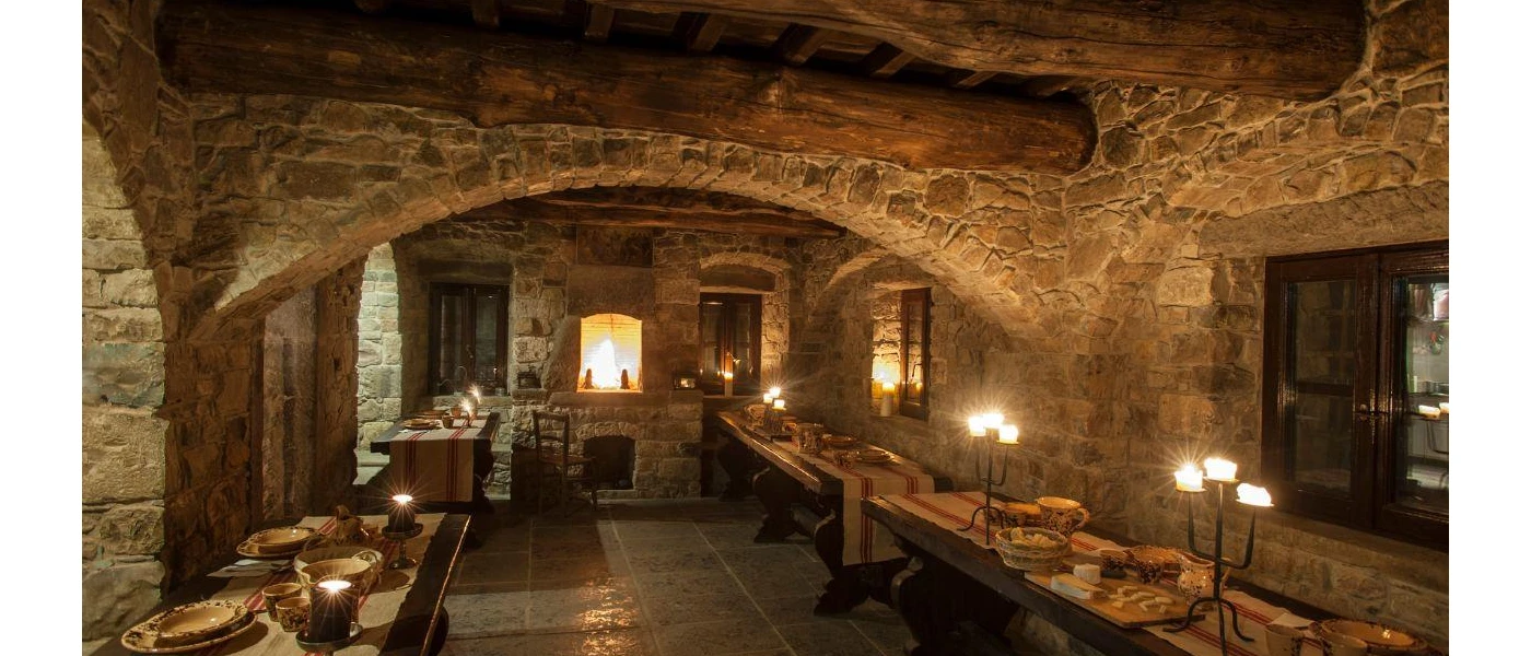 Restaurant with stone walls and ceilings, wooden beans and tables laid up, lit by candlelight