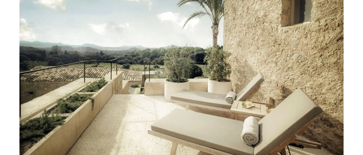 Neutral cushioned loungers next to a stone wall in a sunny terrace, with a view of the surrounding countryside