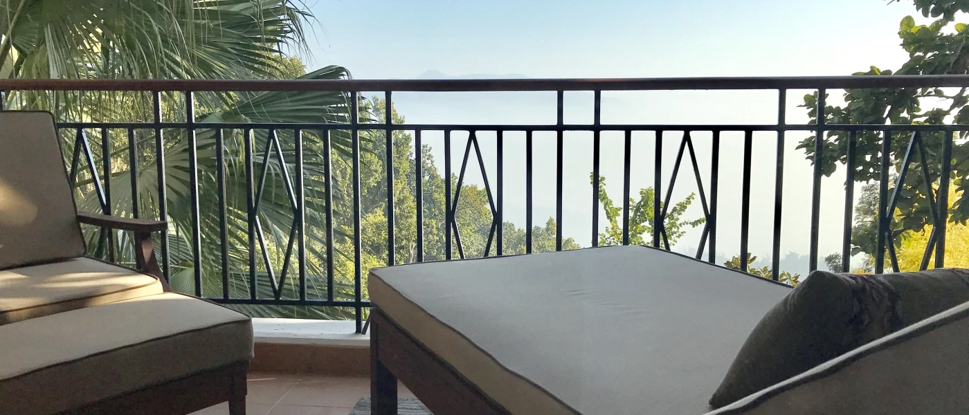 Balcony with black railings, with a cushioned lounger looking over a hillside cloaked in greenery