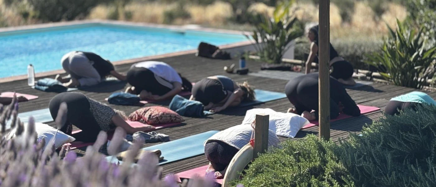 Group on yoga mats in flow on a poolside terrace surrounded by gardens