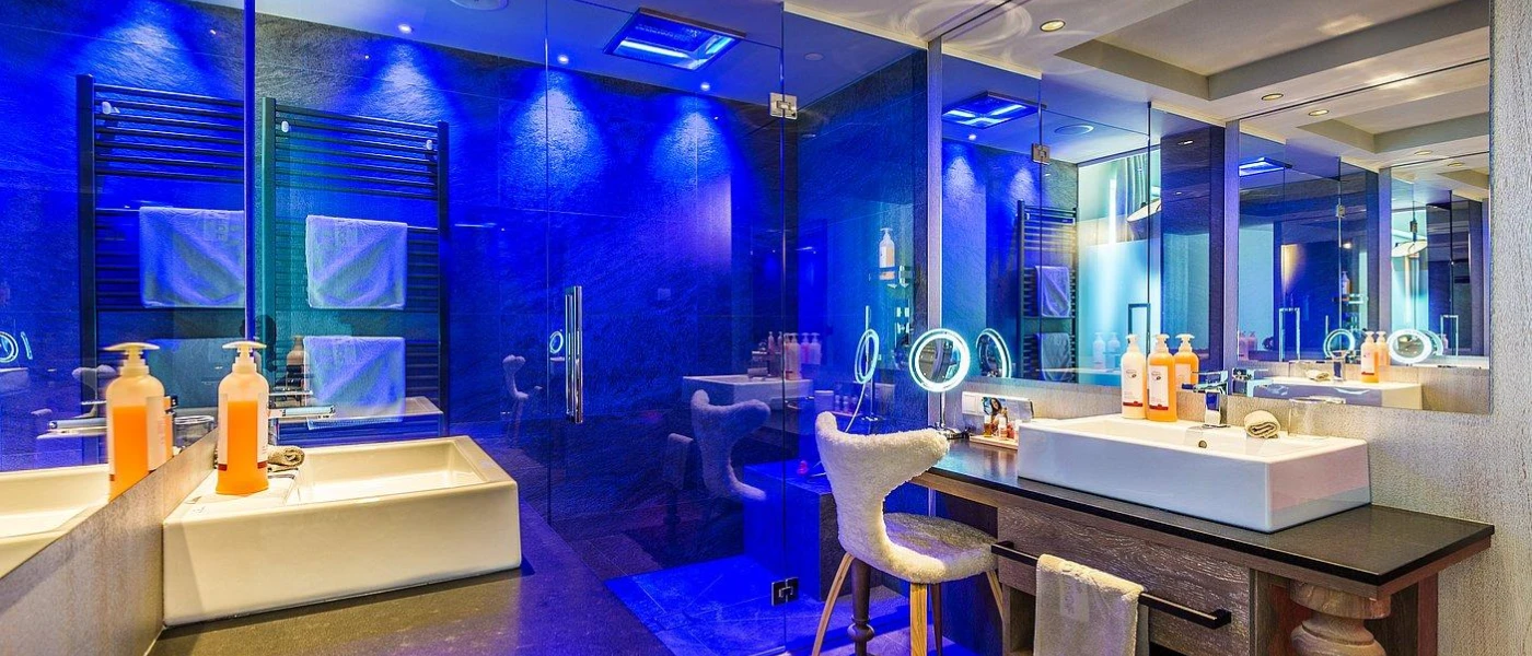Modern bathroom with a huge shower, blue lighting, twin wooden vanity units and a boucle chair 