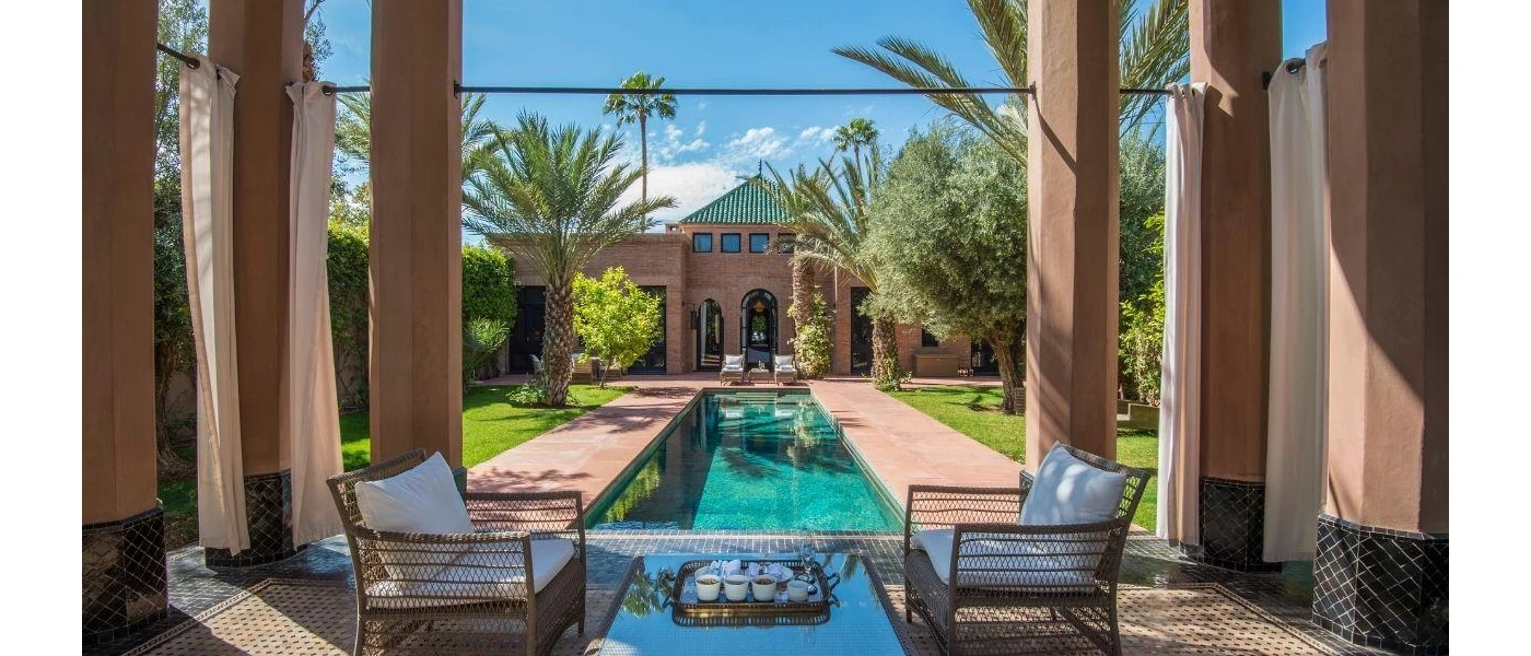 Terrace with pillars and chairs overlooking an outdoor swimming pool and gardens with palm trees