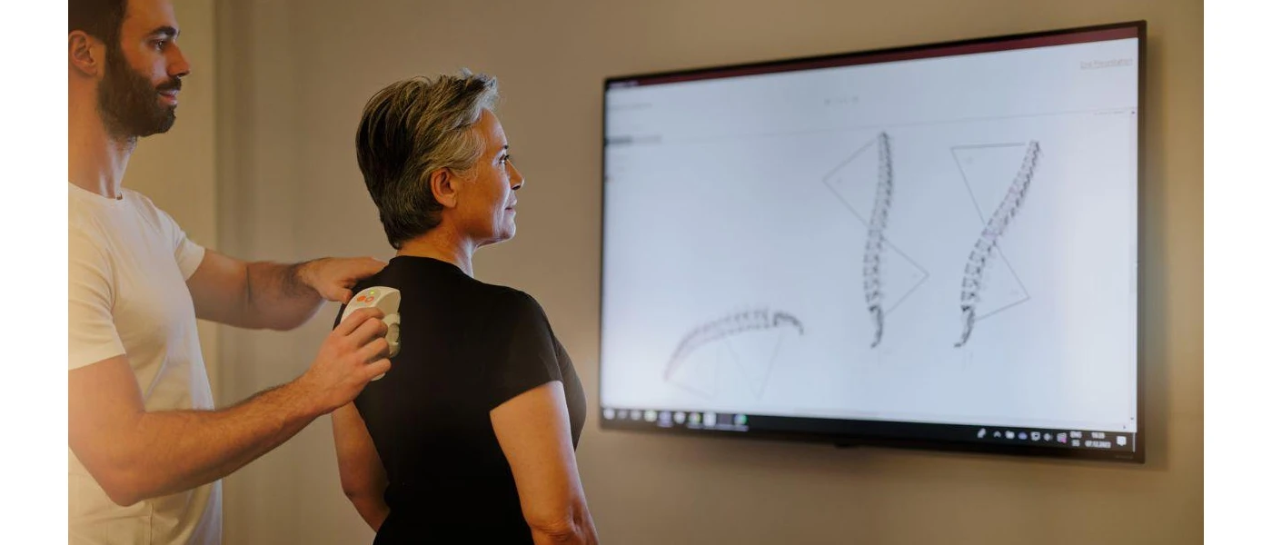 Woman in a black t shirt watching a screen showing images of the spine as a healthcare expert runs a machine down her black