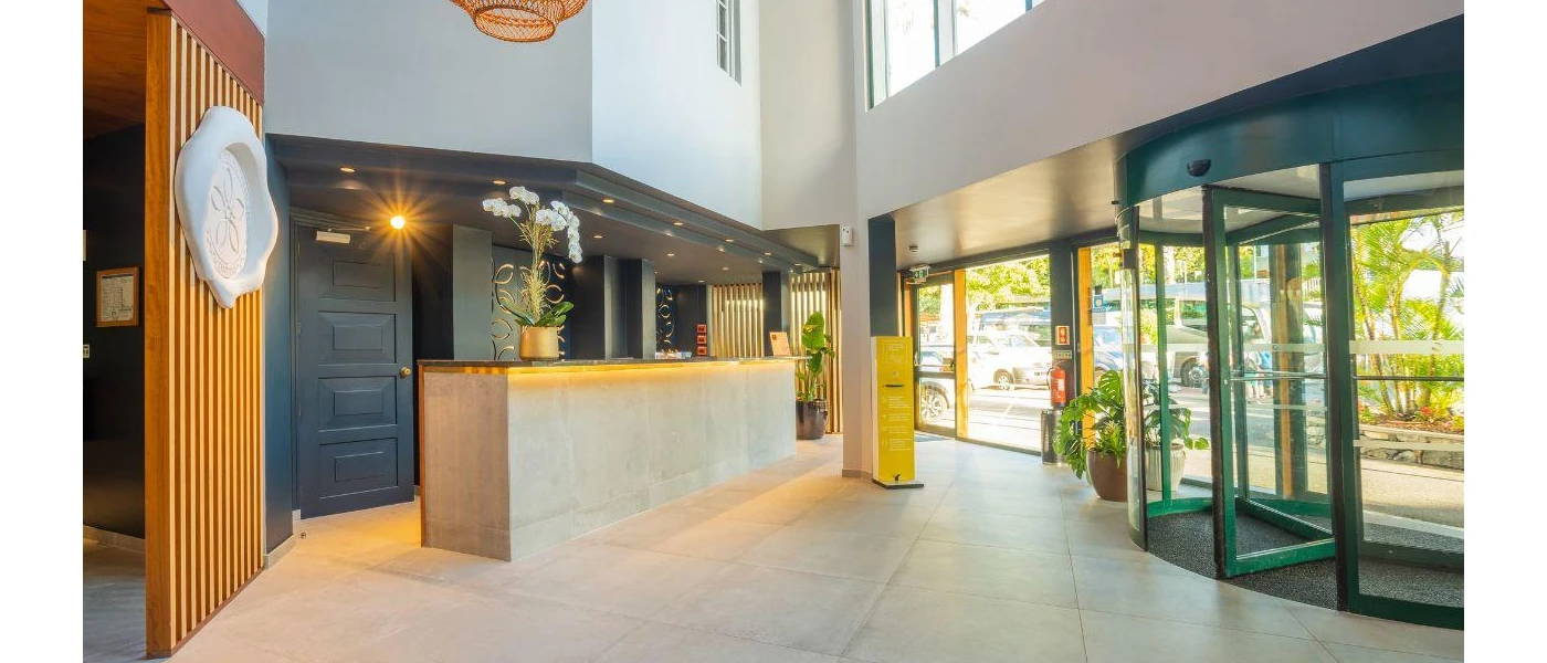 Modern reception area with revolving doors, tiled floors, and a desk with spotlights and a huge potted plant