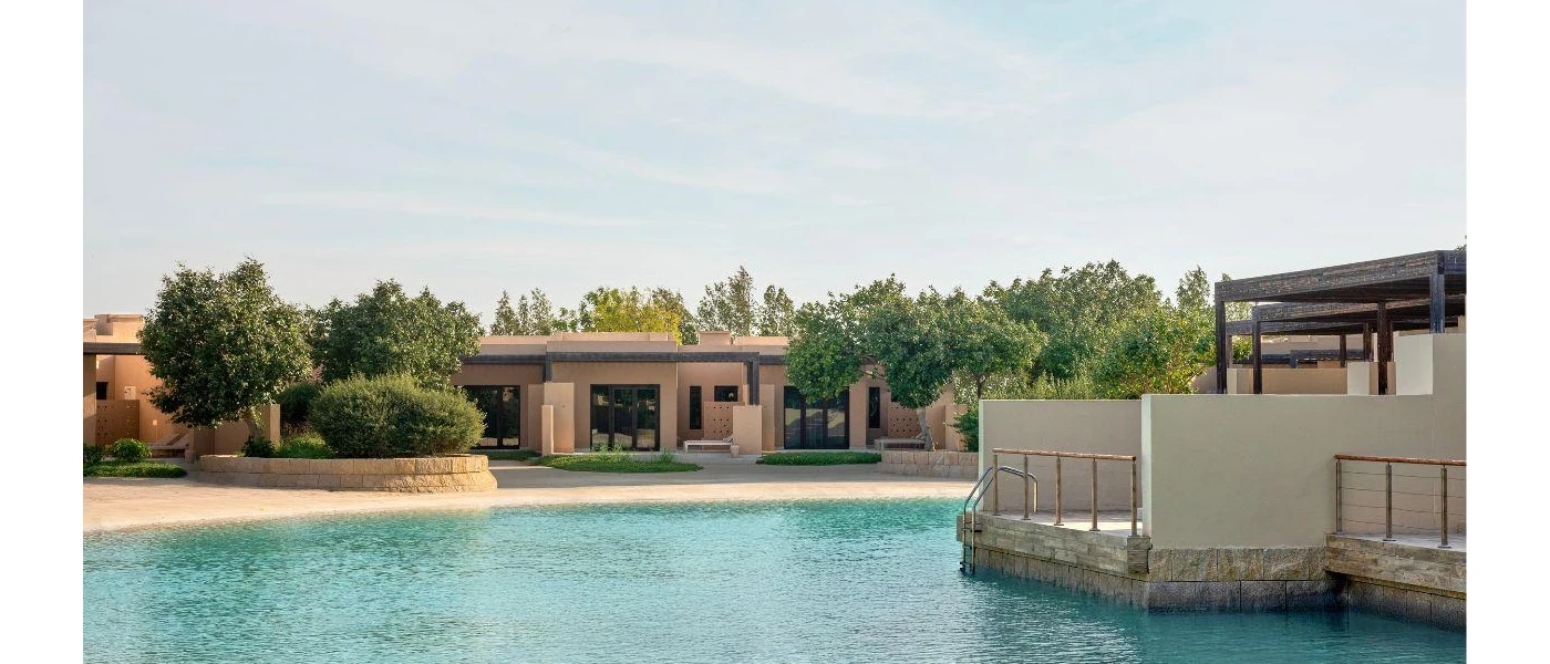 Swimming pool with a shelving shoreline design surrounded by low-rise sand-coloured buildings