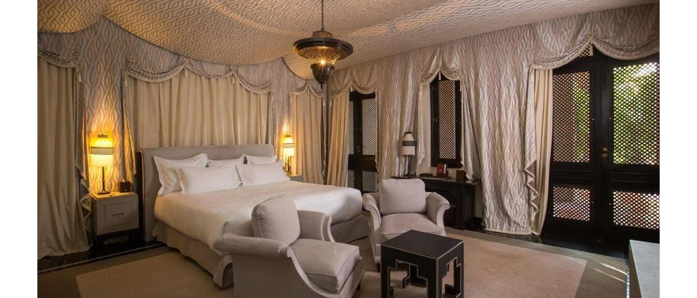 Stylish bedroom with white bedding, white drapes, grey chairs and a black side table