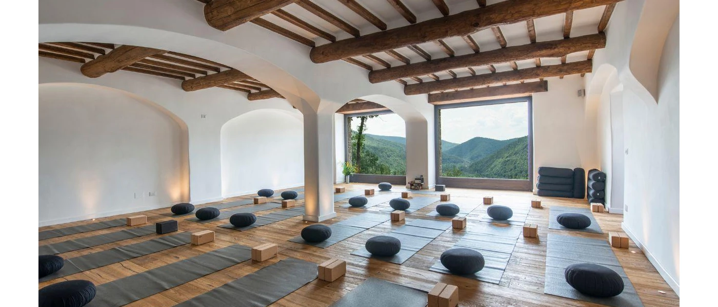 Large room with cushions and yoga mats lined up, and a window with a view of green hills outside