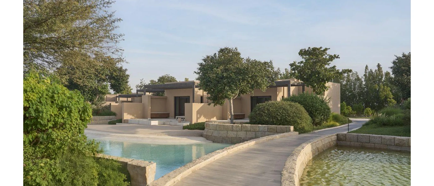 Sand-coloured cube-shaped buildings among gardens, pathways and a swimming pool with a gently shelving design