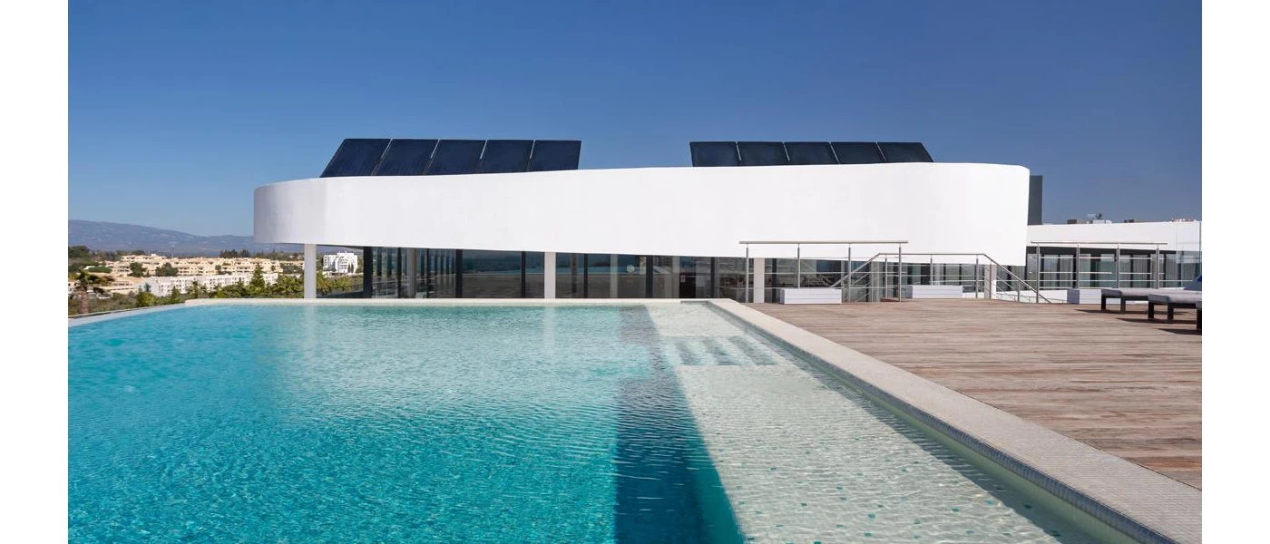 Corner of a swimming pool on a wooden decked rooftop terrace, with a white rooftop of a restaurant behind