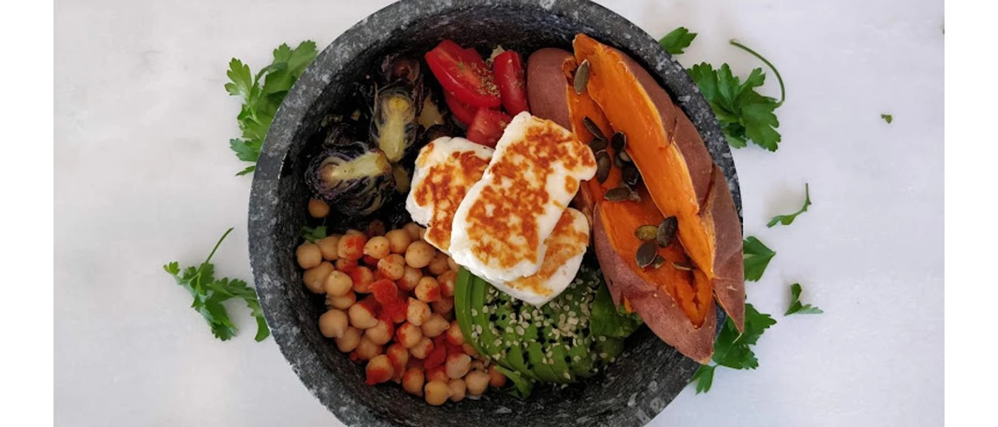 Dark bowl with sweet potato and seeds, chick peas, halloumi and avocados and tomatoes