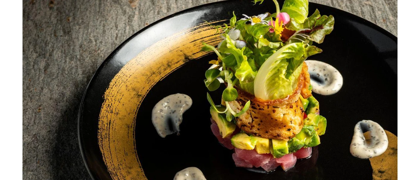 Black plate with a tower of seafood or meat, avocado, salad and edible flowers