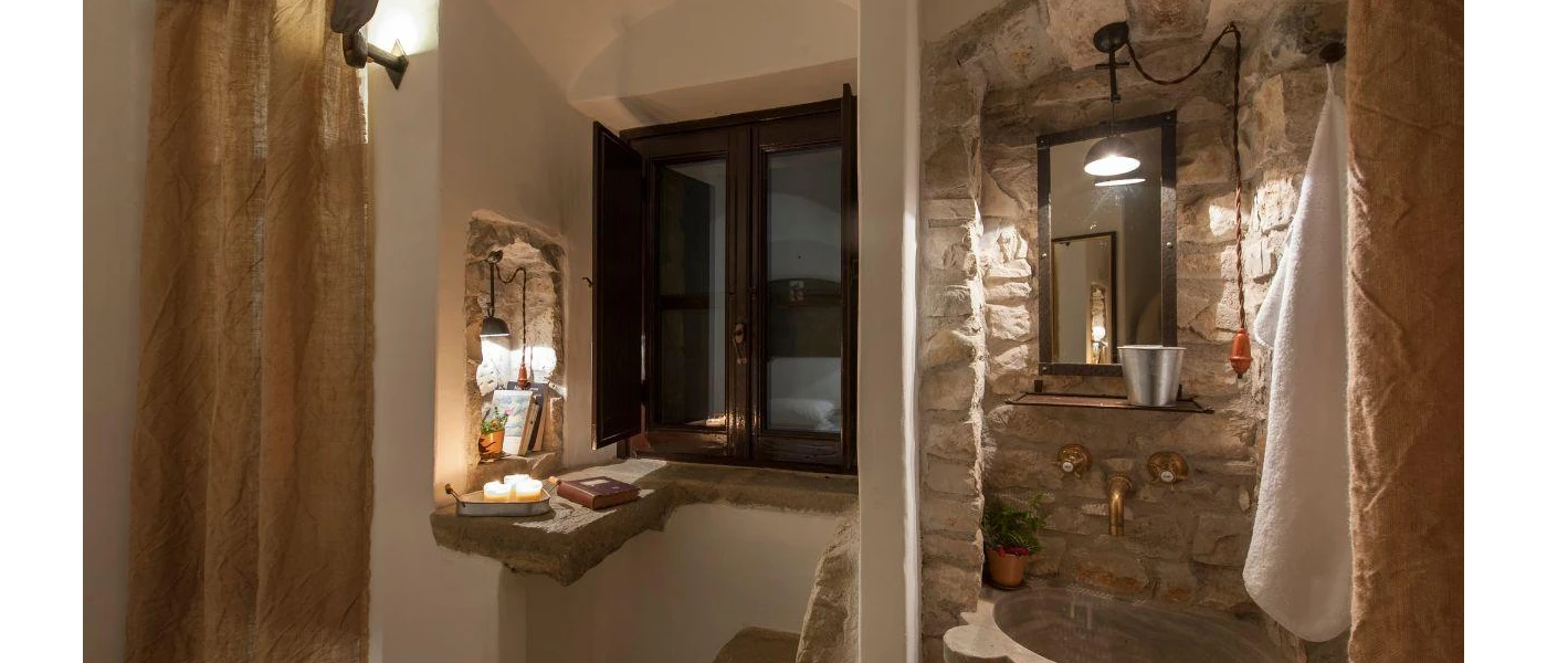 Stone shower area with white curtain and desk next to a small dark-wood window