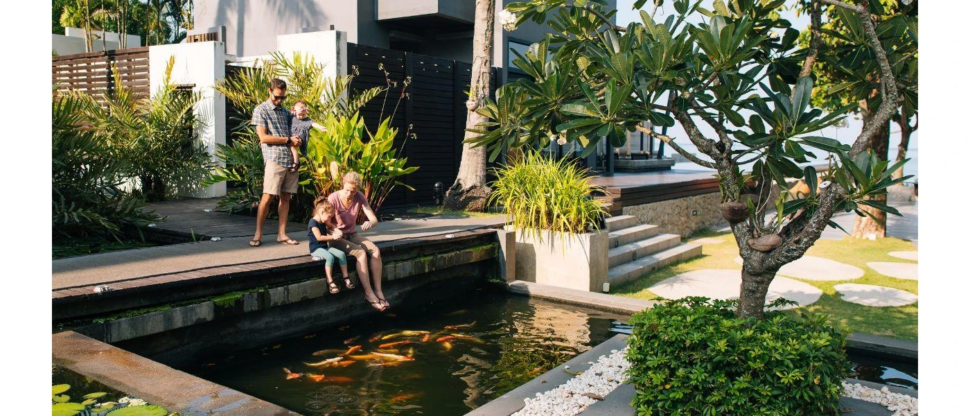 Family dangle their feet over a fish-filled pond among tropical grounds
