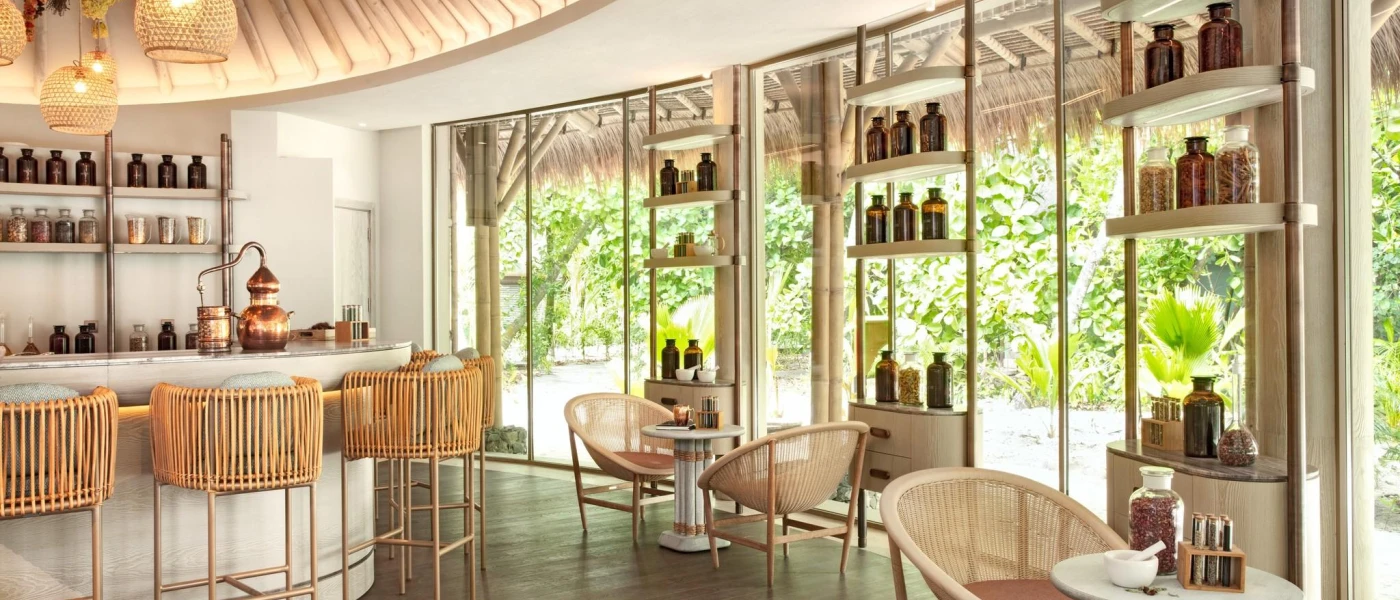 Circular room with floor-to-ceiling windows, shelves stacked with jars and bottles and rattan stalls huddled around a central bar area