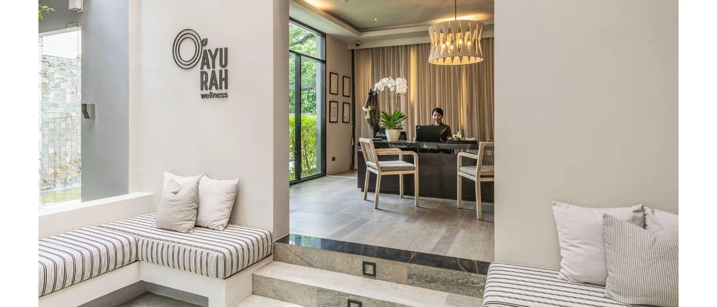 Spa entrance, with tiled and wood flooring, neutral sofas and a desk with a smiling staff member sat behind
