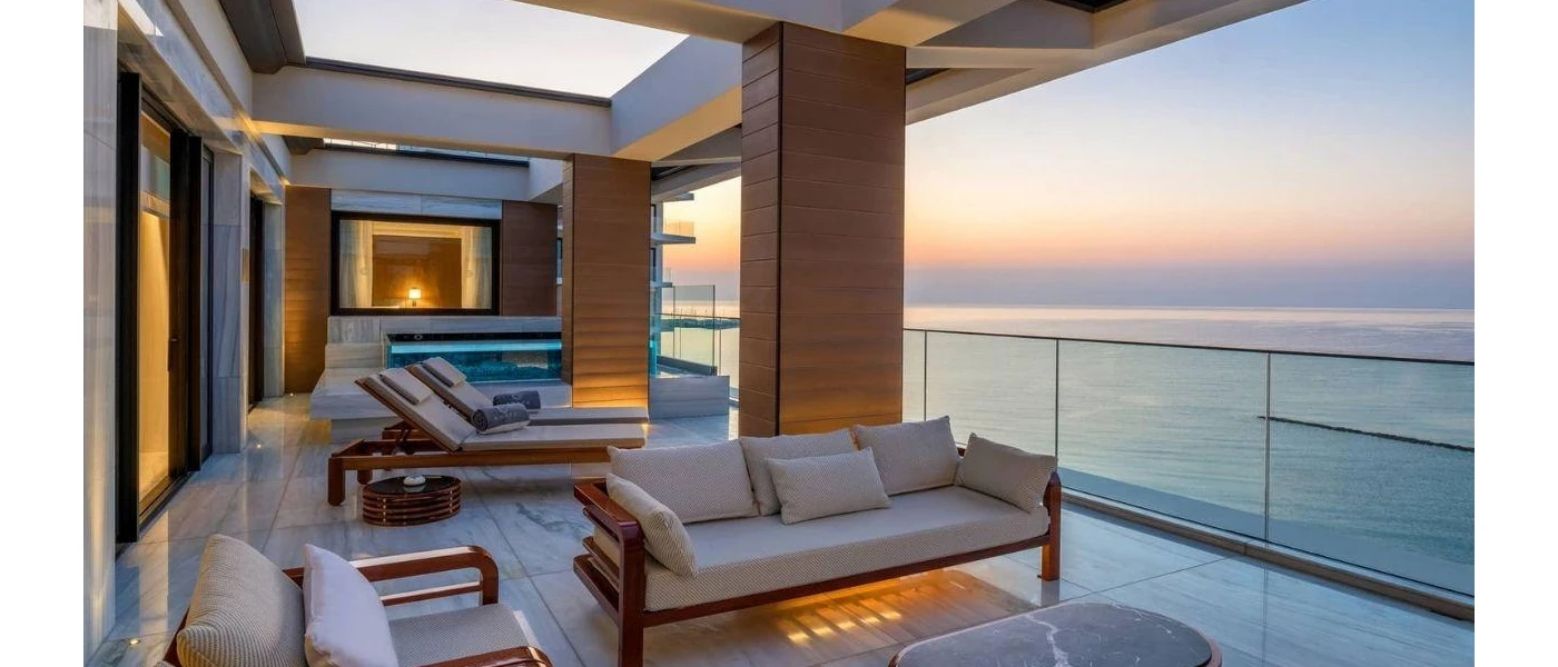 Outdoor terrace with neutral-coloured cushioned loungers and seating and a square swimming pool overlooking the sea