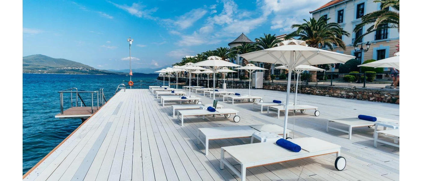 Seafront terrace with white wooden decking, loungers and umbrellas and blue towels under a blue sky