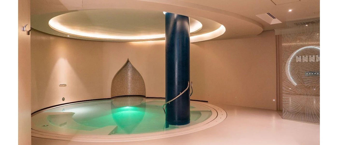 Circular indoor pool with a black pillar support, in a room with a circular ceiling design and LED lighting