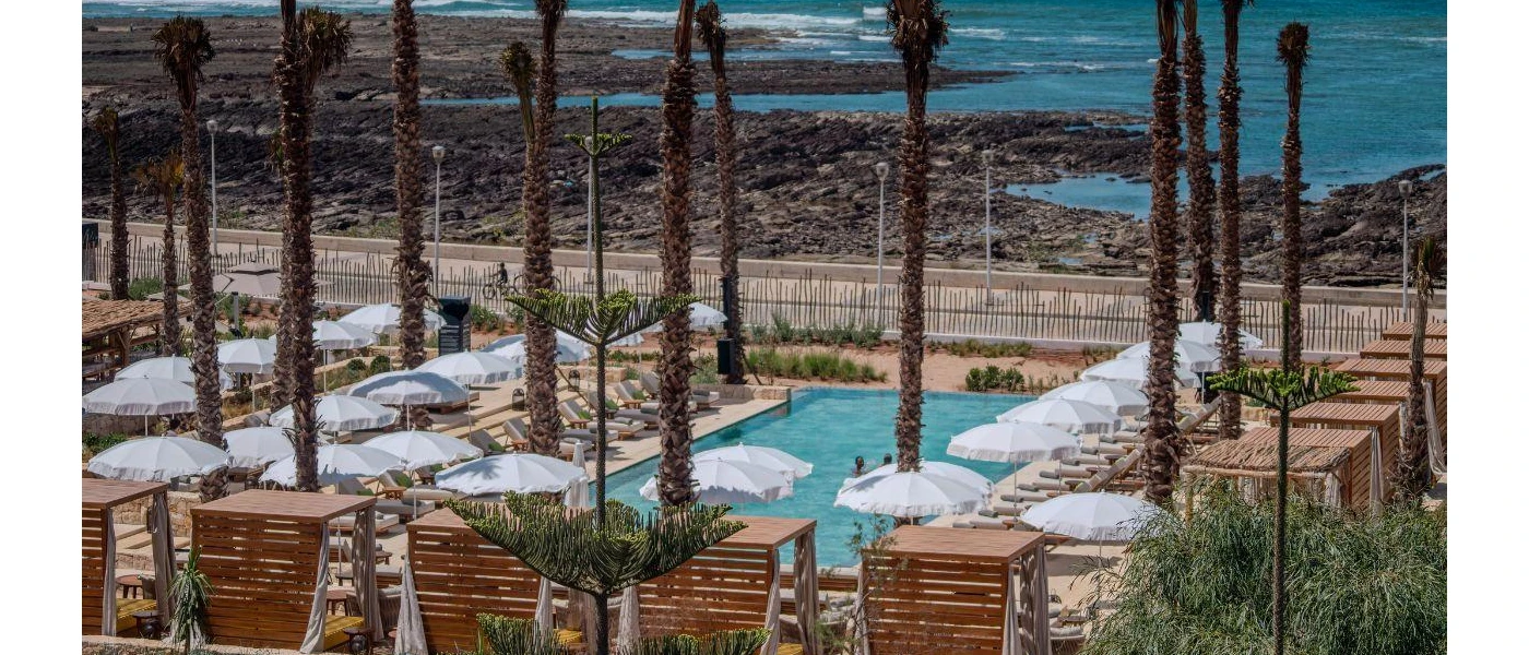 Sea-facing swimming pool surrounded by white umbrellas and tall palm trees